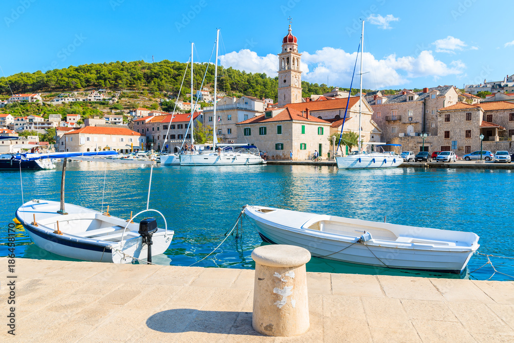 Fototapeta premium Fishing boats in Pucisca port with beautiful church in background, Brac island, Croatia