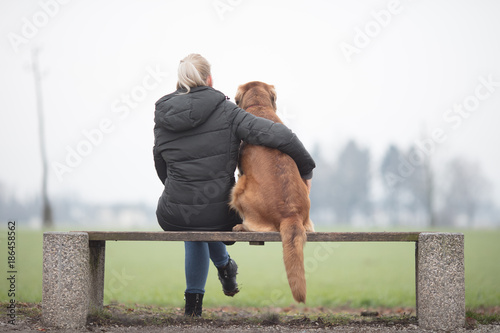 beautiful dog owner with her big  brown dog, sitting on a bank and looking into the future