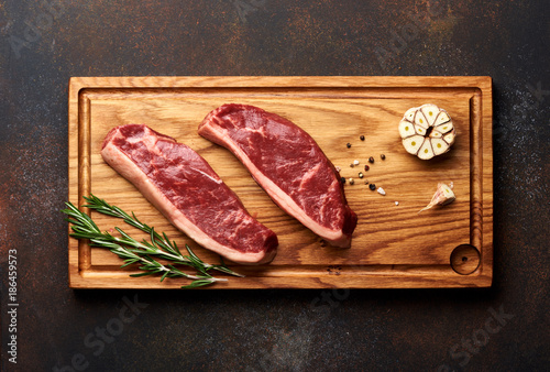Raw fresh meat Picanha steak, traditional Brazilian cut with rosemary and garlic and black pepper on wooden board. Sliced meat steaks. Top view.