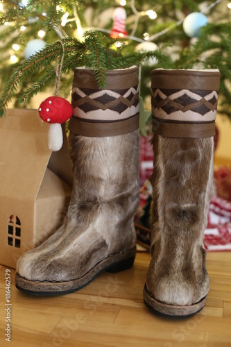 a pair of warm boots in wool stands near the Christmas tree on a wooden floor.