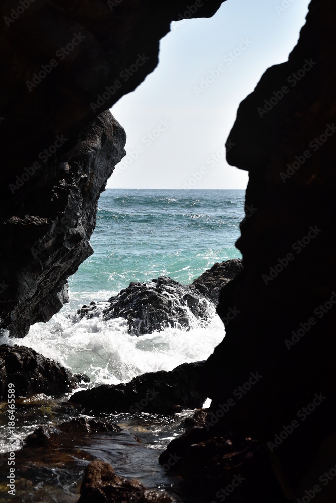 Blue water seascape spray on rocky coast through a stone niche