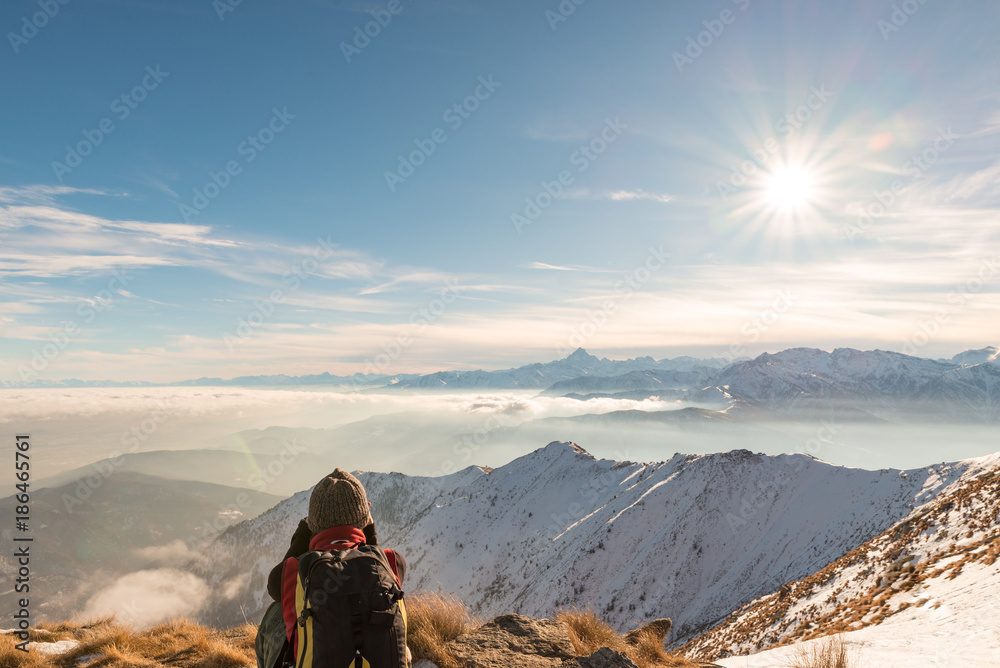 Woman backpacker resting on mountain top. Rear view, winter lifestyle, cold feeling, sun star in backlight
