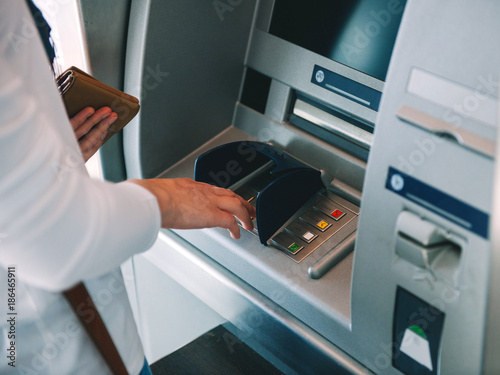 Woman using ATM holding wallet an pressing the PIN security number on the keyboard automatic teller machine 