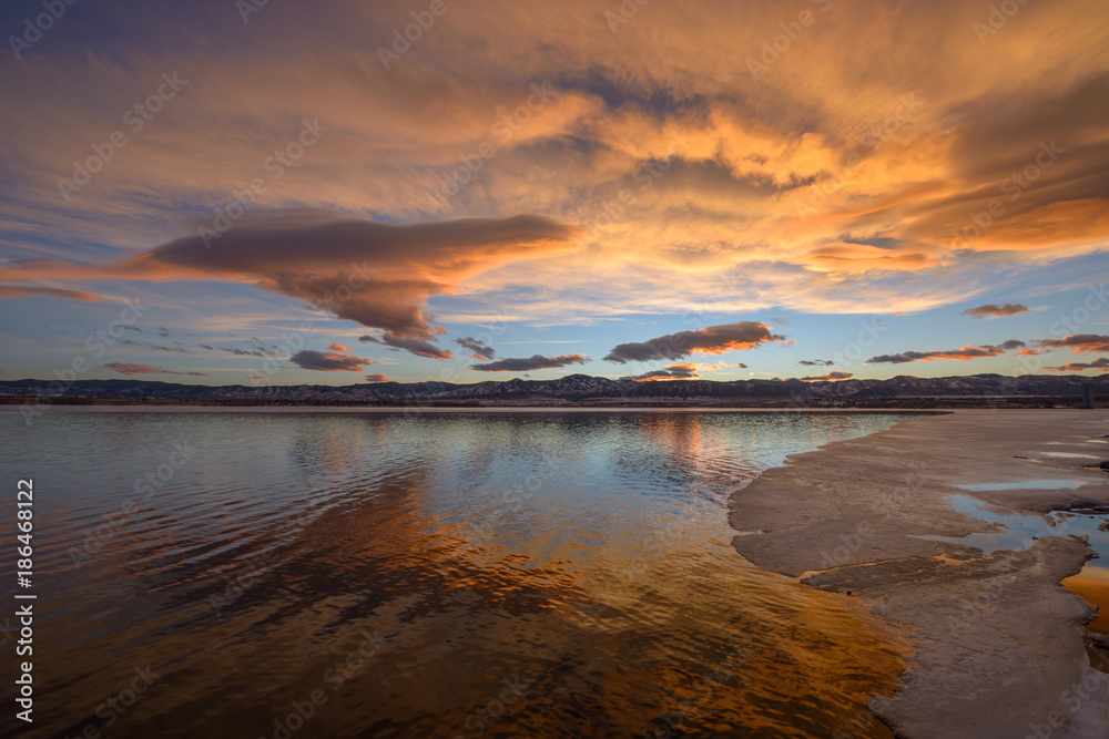 Sunset Spring Mountain Lake - Panoramic colorful sunset view of spring storm clouds rolling out rocky mountains front range and passing over an ice-melting lake.