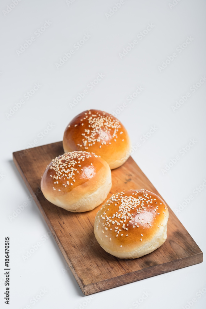Tasty buns with sesame on oven-tray, on wooden background.