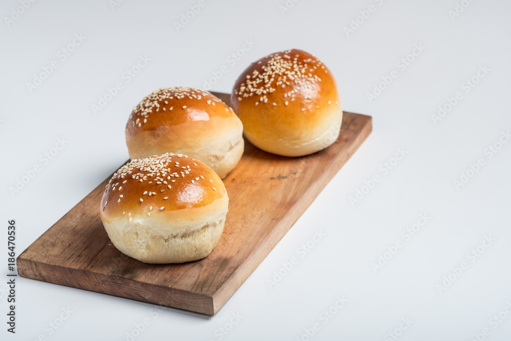 Tasty buns with sesame on oven-tray, on wooden background.