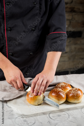 Cooking bread buns for burger on wooden table by chef hands. White isolated background.