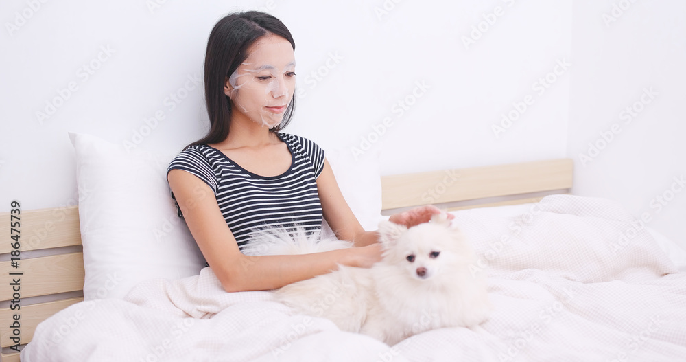 Woman apply paper mask on bed and play with her dog Woman apply paper mask on bed and play with her dog