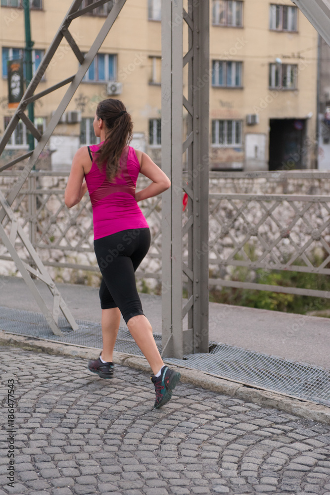 woman jogging across the bridge at sunny morning