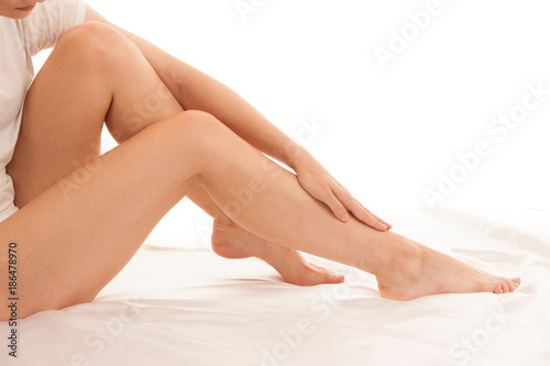 Long and slim woman legs on white sheets in bed isolated over white background