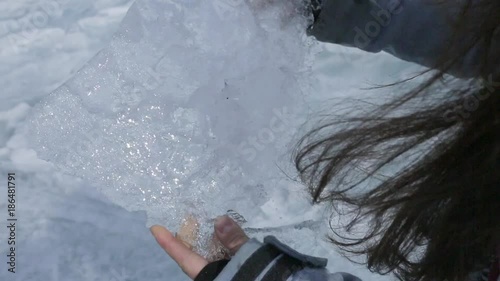 The woman holds the rubber ice in her hands and moves it, making it shine on the sun. The surface of the block is irregular and the defrost water glistens and sparkles brightly on the light. The lady