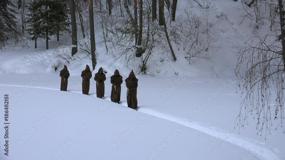 Group of monks in hood robe walking along winter snow trail in forest