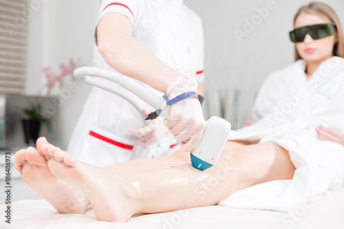focus on the patient's face. Doctor cosmetologist makes the procedure a young girl blonde. Laser epilation and cosmetology. Hair removal on ladies legs. at cosmetic beauty spa clinic.