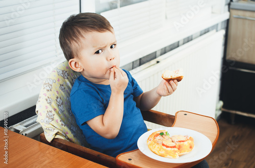 The little boy in the kitchen eating a small pizza photo