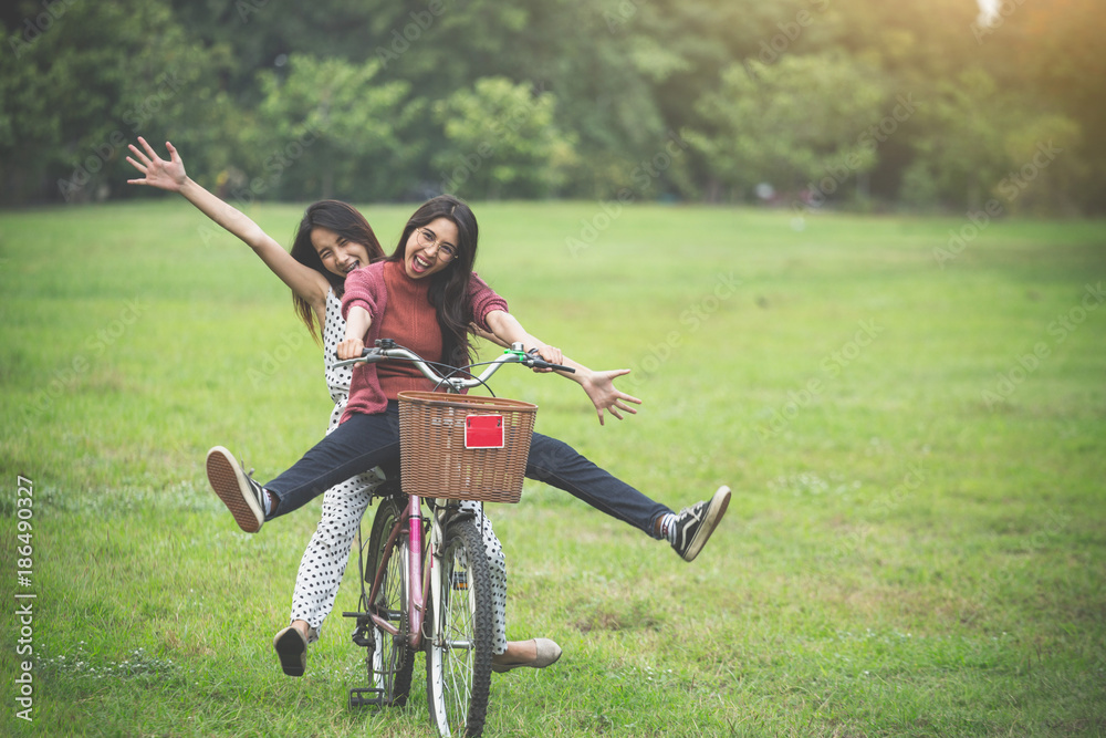 Fototapeta premium Girls ride a bicycle in park, having fun by play together