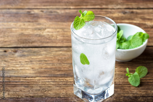 Glass of water with ice and mint on wooden background.