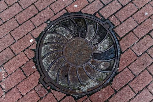 Round metal hatch in urban pavement, sewer manhole cover with marking lines
