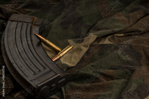 Foto Rusty AK-47 magazine and bullets on camouflage textile background