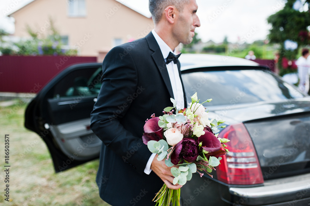 Portrait of a handsome groom walking out of the car with a wedding bouquet in his hands. Portrait of a handsome groom walking out of the car with a wedding bouquet in his hands.