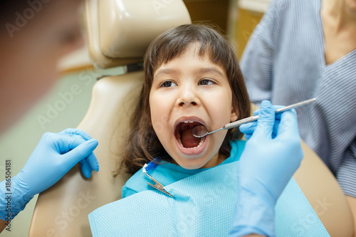 Little girl is having her teeth examined by dentist