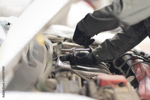 Mechanic using a wrench and socket on the engine of a motor car during a service or repair in an automotive workshop, close up of his hands