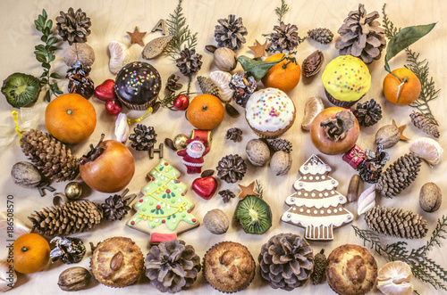 Christmas cookies,toy Santa Claus,fruits,nuts, pine cones with chocolate sweets on a plywood table