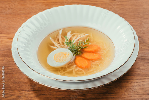 Chicken soup with vegetables and egg in white plate on wooden table