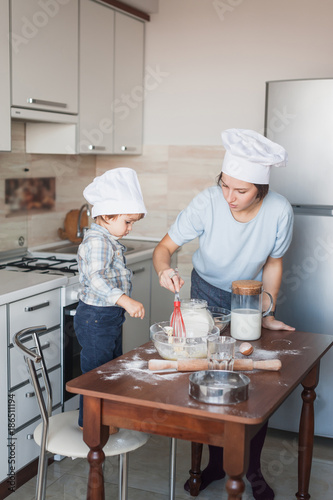 mother and adorable little child mixing dough with whisk at kitchen