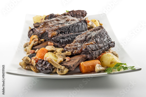 White rectangular plate with three cooked beef ribs mushrooms carrots and potatoes