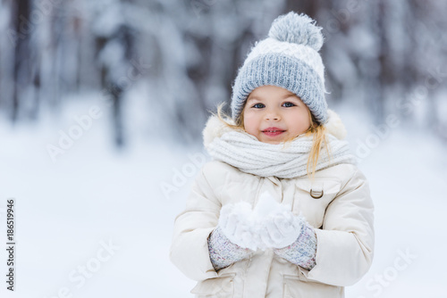 portrait of adorable kid holding snow ball in hands in winter park