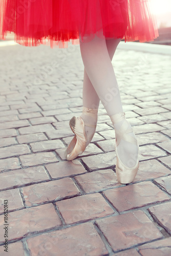 Ballet dancer's feet dancing on street. Young ballerinas in red tutu. Ballet feet on the point on red brick.