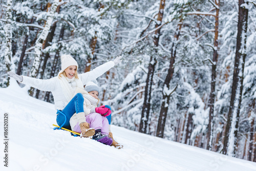 happy daughter and mother sledging together in winter park