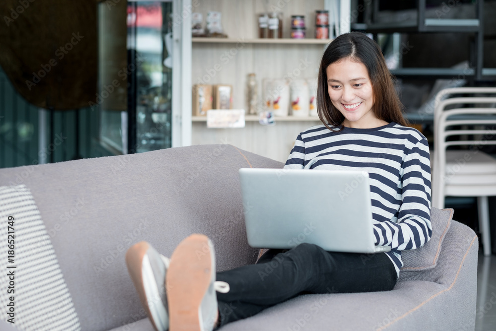 Asian teenager girl using laptop computer and sitting cross legs on sofa with happy smiling face at coffee shop,Digital age lifestyle.blogger influencer review.live video chat.working outside office.