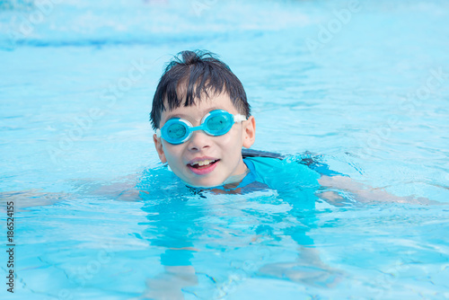 Young asian boy wearing goggles swimming in outdoor swimming pool