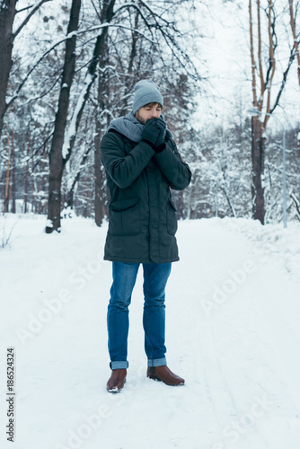 young man warming hands up while walking in snowy park
