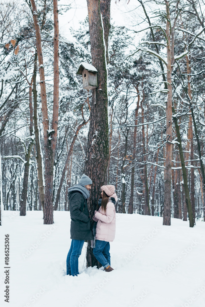 young couple looking at each other while standing in winter forest young couple looking at each other while standing in winter forest