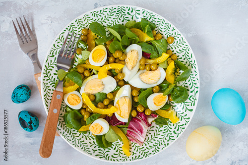 Spring Easter salad with chicken and quail eggs, lettuce corn, pepper, painted eggs. Top view, copy space. Easter concept.