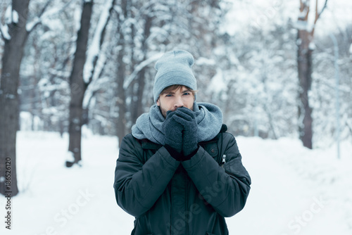 portrait of young man warming hands up while walking in snowy park