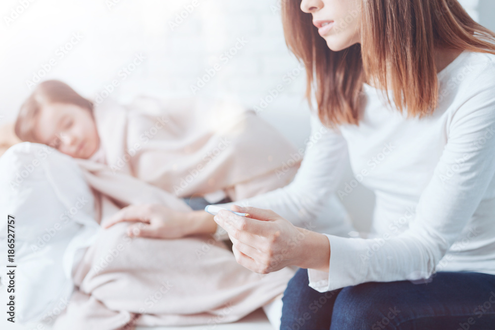Do not worry. Young female person leaning elbows on the knees while holding thermometer in left hand and thinking how to treat her child Do not worry. Young female person leaning elbows on the knees while holding thermometer in left hand and thinking how to treat her child