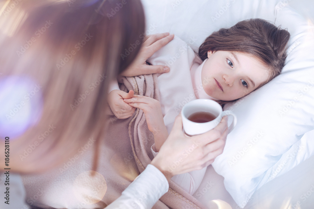 Do not be so serious. Kind brunette female sitting near her child while giving cup with tea to make her feel better Do not be so serious. Kind brunette female sitting near her child while giving cup with tea to make her feel better