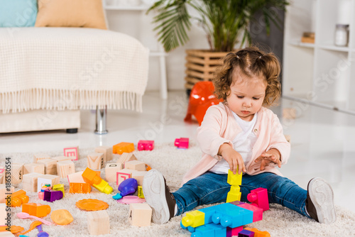 adorable child playing with plastic blocks on floor