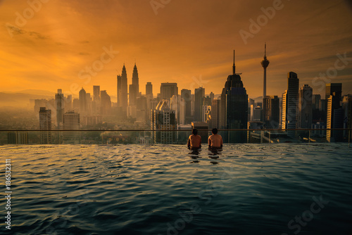 Two traveler man looking view skyline Kuala Lumpur city in swimming pool on the roof top of hotel at sunrise in Kuala Lumpur, Malaysia.