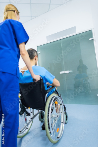 back view of surgeon and male patient in wheelchair in hospital corridor