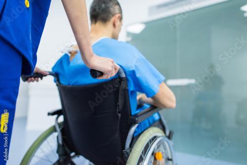 rear view of surgeon and male patient in wheelchair in hospital corridor