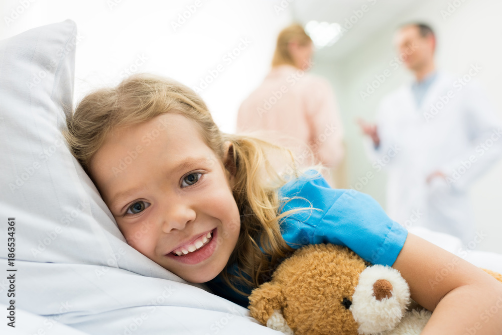 happy kid lying on hospital bed while mother talking with doctor happy kid lying on hospital bed while mother talking with doctor