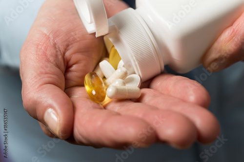 Woman pours from a white bottle into palm hand the variety medication pills, yellow capsules of omega 3, glucosamine and calcium dietary supplements