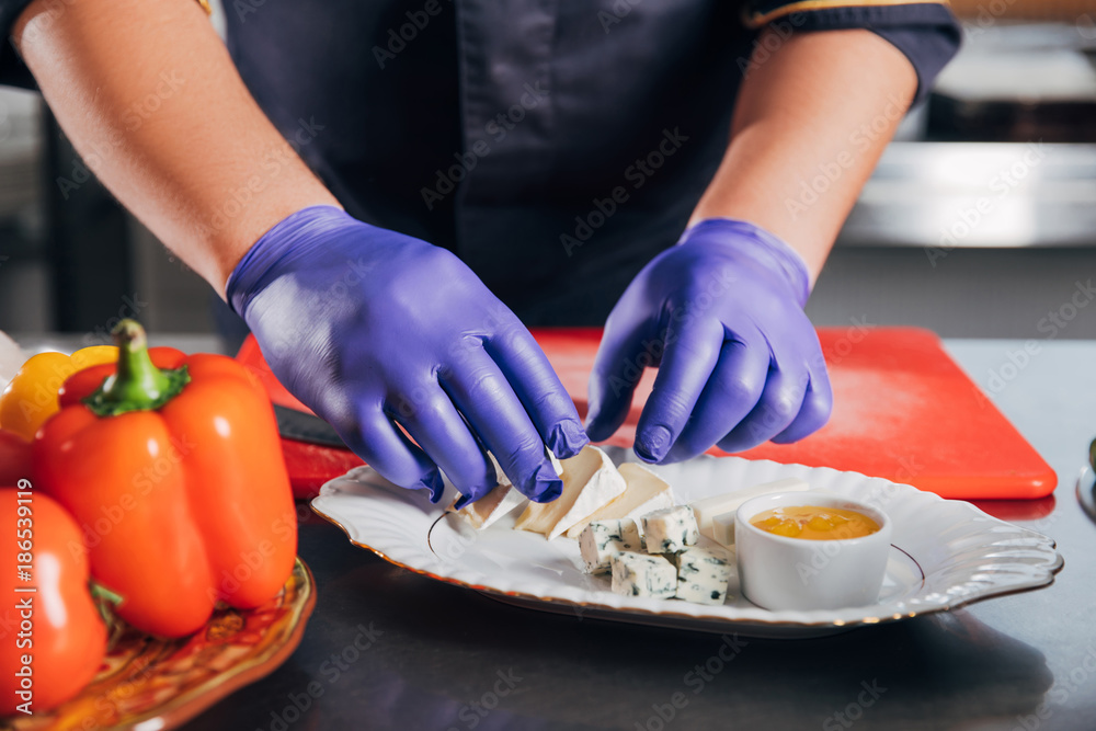 cropped shot of chef putting cheese slices on plate at restaurant cropped shot of chef putting cheese slices on plate at restaurant