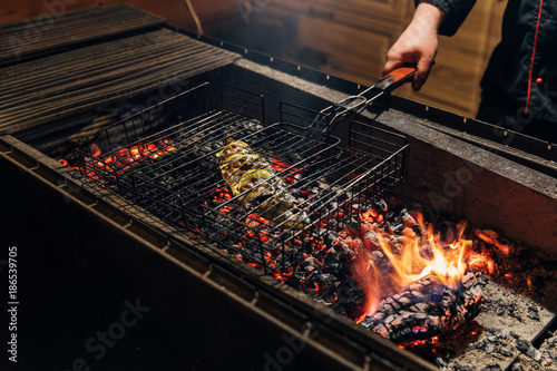 cropped shot of chef grilling fish on flame in restaurant