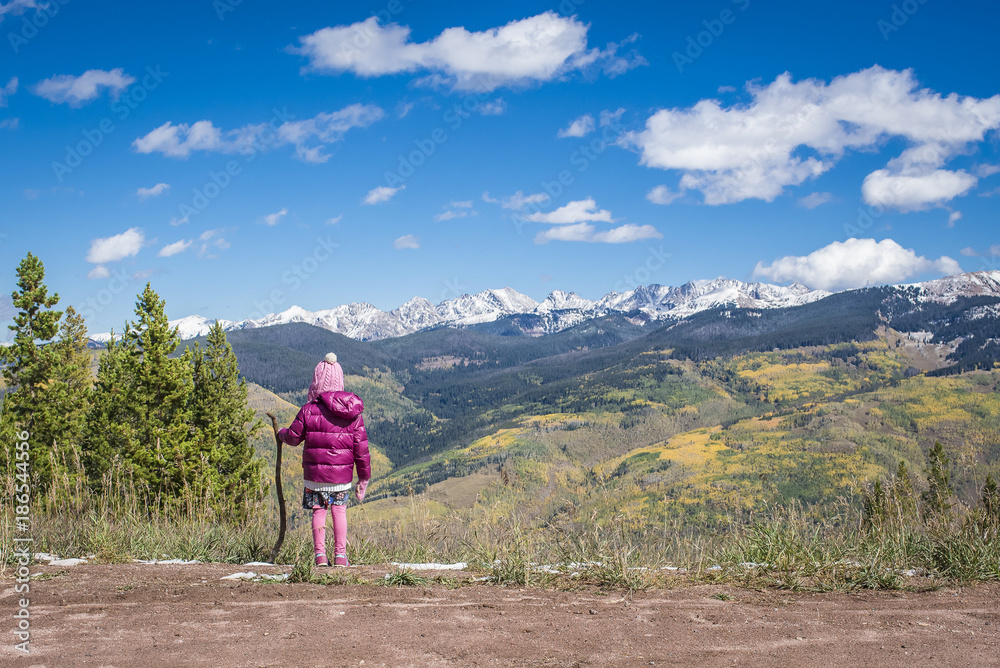 Rear view of girl in warm clothing with stick standing on mountain against sky Rear view of girl in warm clothing with stick standing on mountain against sky