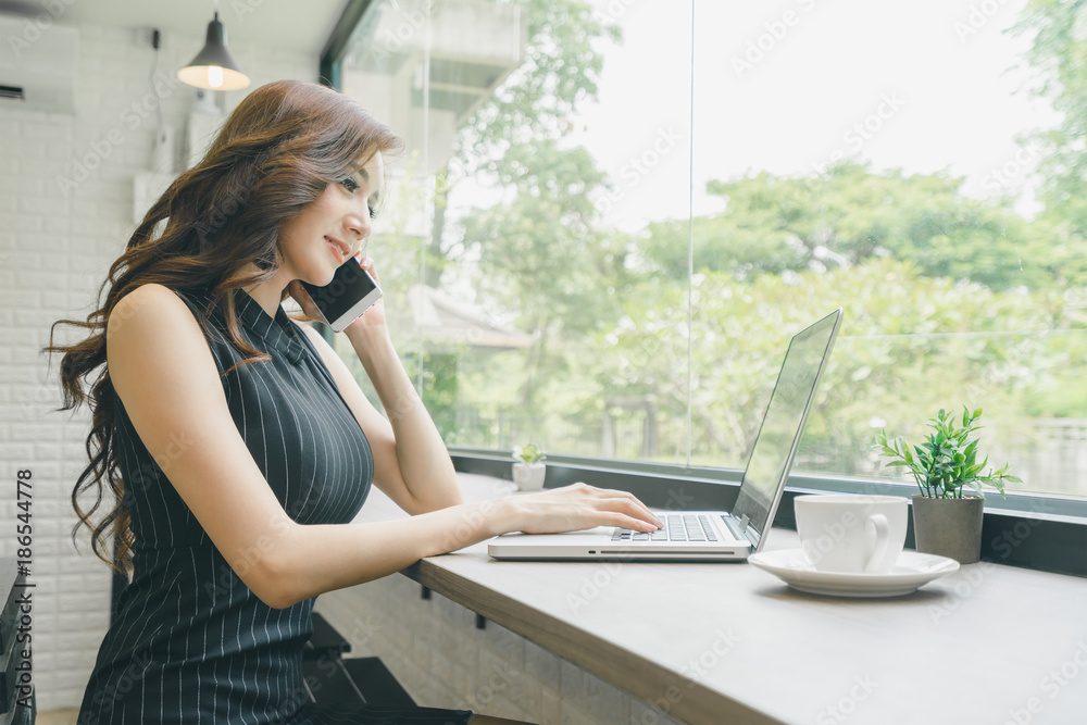 Beautiful young Asian businesswoman using smartphone and working with laptop in the coffee shop Beautiful young Asian businesswoman using smartphone and working with laptop in the coffee shop